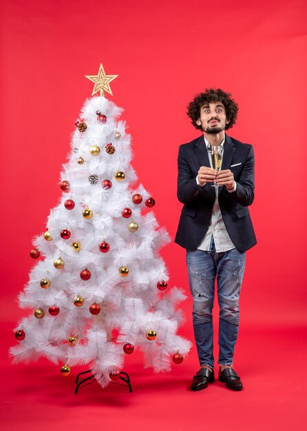 New year celebration with young man giving a glass of wine and standing near decorated white Christmas tree