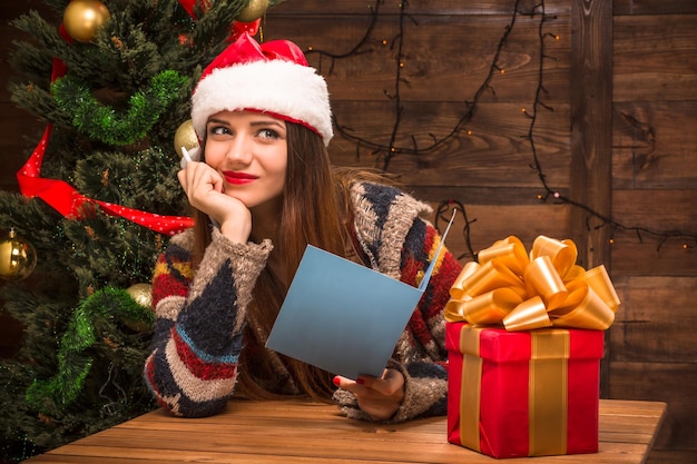 New Year and Christmas concepts. Beautiful girl holding a New Year and Christmas post card and smiling. Nice presents standing in front of her.