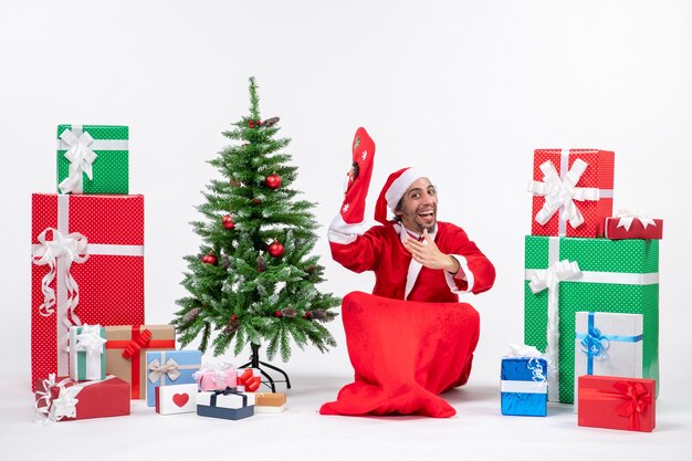 New year mood with santa claus sitting on the ground and wear christmas sock near gifts and decorated Xmas tree on white background stock photo