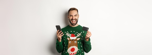 New year online shopping and christmas concept excited man using credit card and smartphone standing