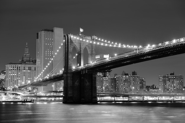 New York City Brooklyn Bridge black and white with downtown skyline over East River.