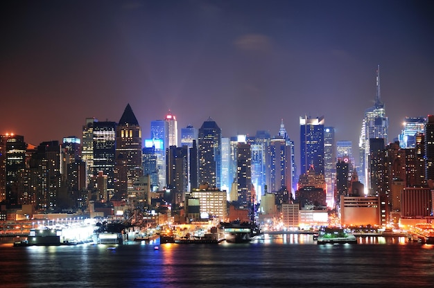 New York City Manhattan midtown skyline at night with skyscrapers lit over Hudson River with reflections.