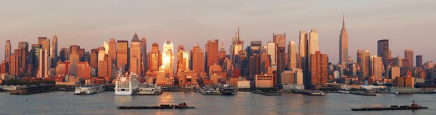 New York City Manhattan skyline panorama at sunset with empire state building and skyscrapers with reflection over Hudson river.