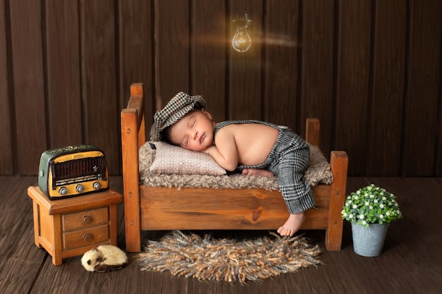 Newborn baby portrait of likeable and pretty baby boy laying on little wooden bed surrounded by flowers radio and cute animal on floor