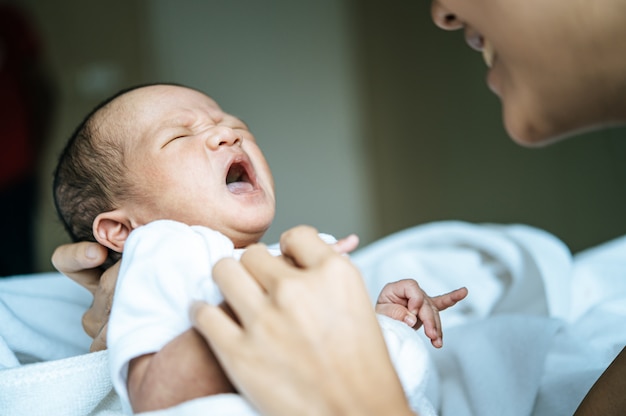 newborn baby wore a white and cried in the arms of the mother