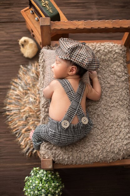 Newborn infant little pretty baby boy laying on wooden bed in baby suit and hat