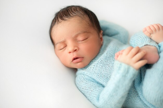 Newborn sleeping baby boy on white chair in cute blue crocheted