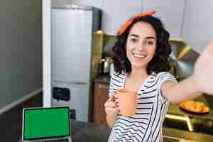 Free photo nice beautiful selfie portrait of amazing joyful happy woman with cut curly brunette hair chilling in kitchen in modern apartment. having fun, drinking tea