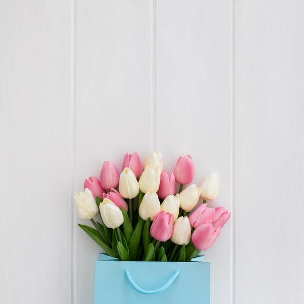 Nice bouquet of tulips inside a blue bag on a white wooden background 