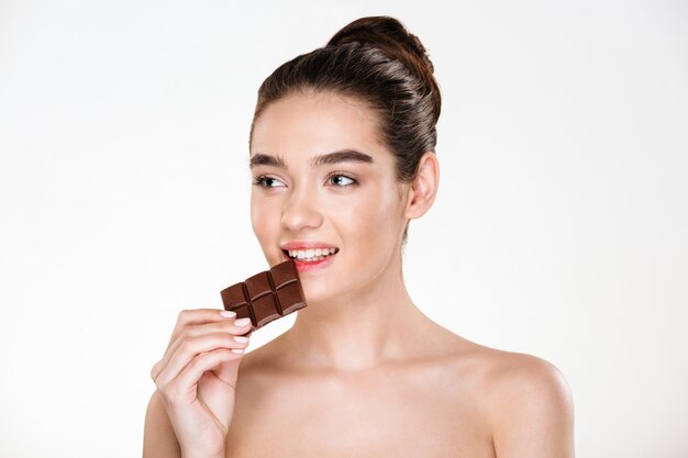 Nice image of hungry half-naked woman with dark hair eating chocolate bar not being on a diet