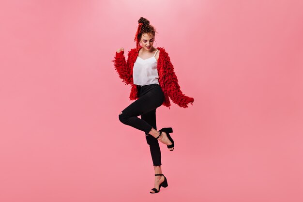 Nice woman in woolen jacket and black pants dancing on pink