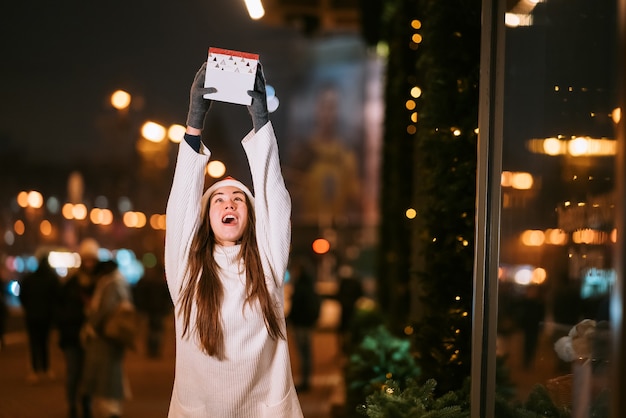 Night street portrait of young beautiful woman acting thrilled. Festive garland lights.