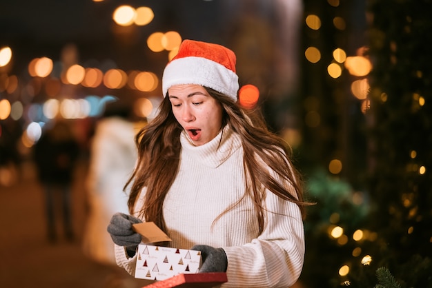 Night street portrait of young beautiful woman acting thrilled. Festive garland lights.