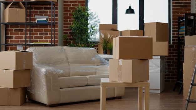 Free photo no people in living room interior to move in with carton boxes, empty real estate property full of cardboard packing storage cargo. nobody in apartment for relocation and moving day.