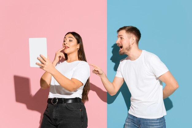 No selfie. He tries to pay her attention. Young, happy man and woman in casual clothes on pink, blue bicolored wall. Concept of human emotions, facial expession, relations, ad. Beautiful couple.