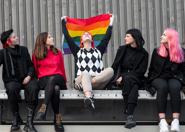 Free photo non binary friends sitting and holding a lgbt flag