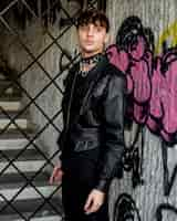 Free photo non binary person in leather jacket posing next to graffiti wall