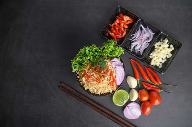 Noodles spicy in the bowl with ingredients and chopsticks on black cement surface, Top view