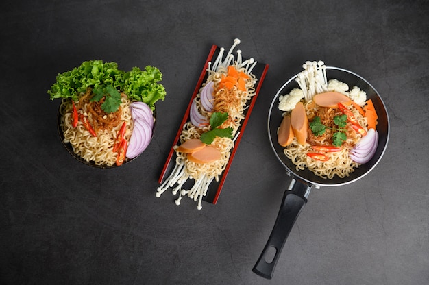 Free photo noodles spicy in wooden tray, frying pans, and bowl with ingredients on black cement surface.