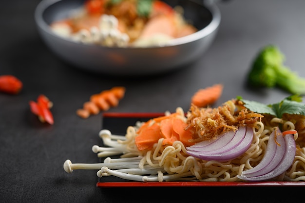 Noodles spicy in Wooden tray with ingredients on black cement surface.