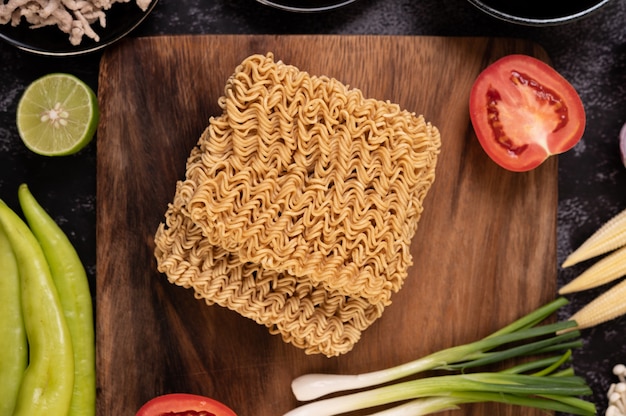 Free photo noodles on a wooden cutting board with tomato, lime, spring onion, chili and baby corn