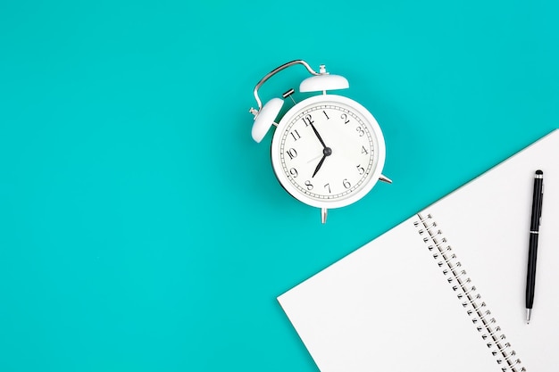 Free photo notebook and alarm clock on a blue background flat lay