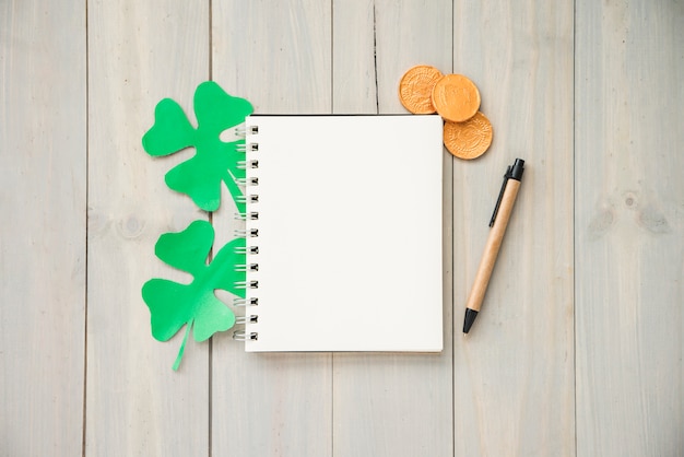 Notebook near coins and decorative clovers