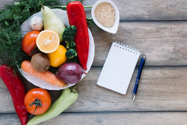 Notebook and pen near fruits and vegetables