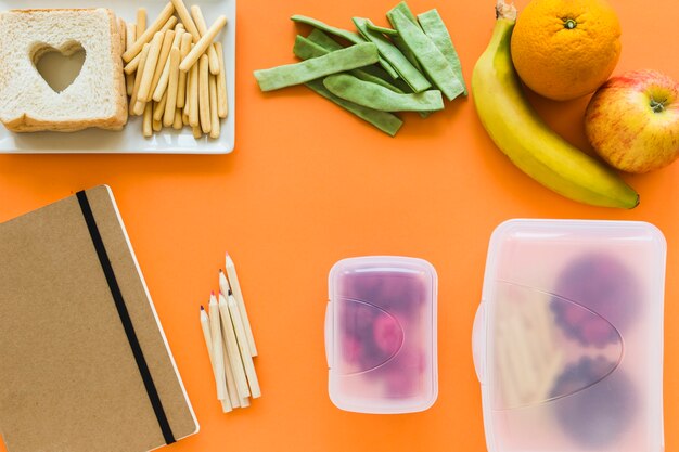 Notebook and pencils near lunchboxes and healthy food