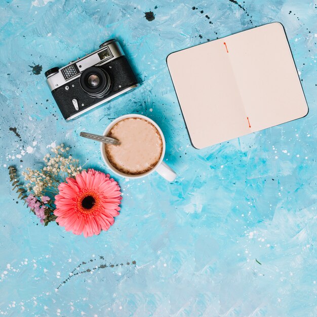 Notebook with camera, coffee and flowers on table 