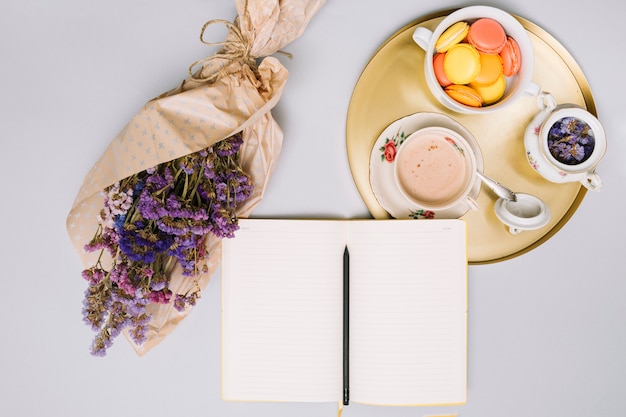 Free photo notebook with flowers bouquet and cookies on tray