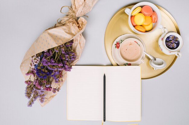 Notebook with flowers bouquet and cookies on tray