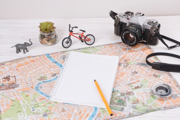 Notebook with pen on map near toy animal, camera and bicycle