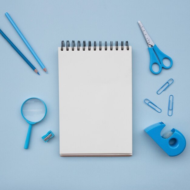 notebook with scissors  magnifying glass pencil sharpener on light blue background