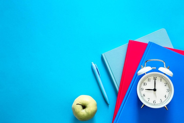 Free photo notebooks pen apple and alarm clock on a blue background top view