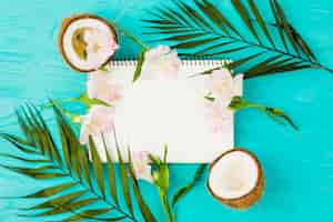 Free photo notepad among plant leaves with fresh coconuts and blooms