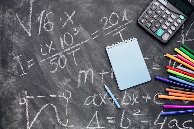 Notepad and calculator with felt pens arranged on written chalkboard