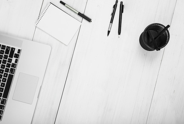 Free photo notepad; pens; holder and laptop on white wooden backdrop