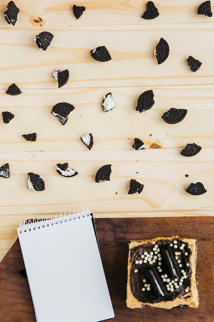 Free photo notepad with pastry near pieces of cookies on wooden table