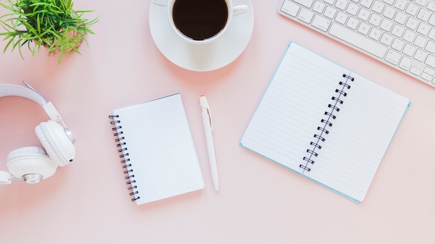 Notepads and coffee cup near headphones and keyboard