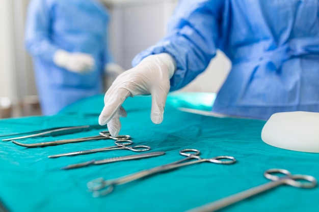 Nurse hand taking surgical instrument for group of surgeons at background operating patient in surgical theatre Steel medical instruments ready to be used Surgery and emergency concept