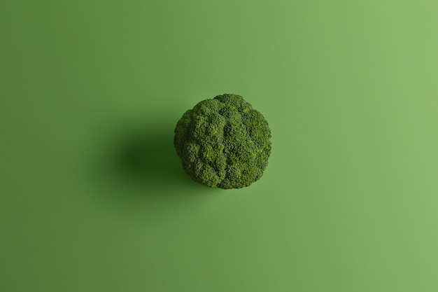 Nutritional healthy broccoli photographed from above on green background. Tasty vegetable can be eaten raw and cooked. Source of vitamins. Cooking and food concept. Nutrient rich type of cabbage