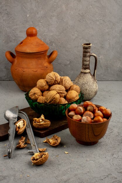 Nuts hazelnuts and walnuts inside brown round pot and green plate surrounded by jugs on a grey floor