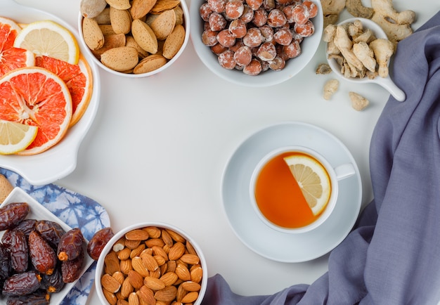 Nuts variety with a cup of tea, dates, citrus fruit slices and ginger in white plates