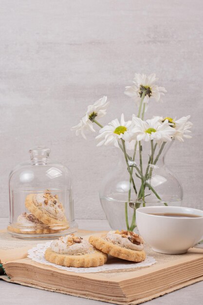 Oatmeal cookies, a cup and daisies on book.