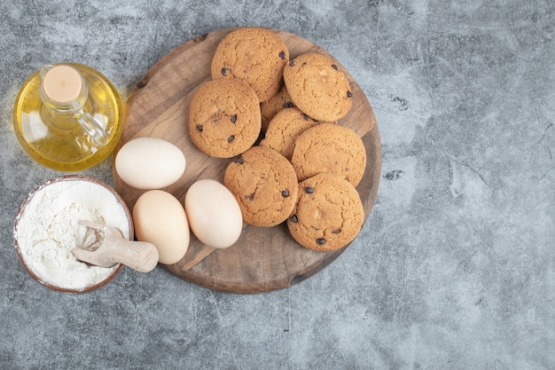 Oatmeal cookies with chocolate drops on a wooden board with ingredients around