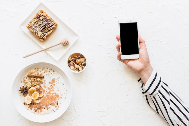 Oatmeals; dryfruits and honeycomb on table with cellphone in hands