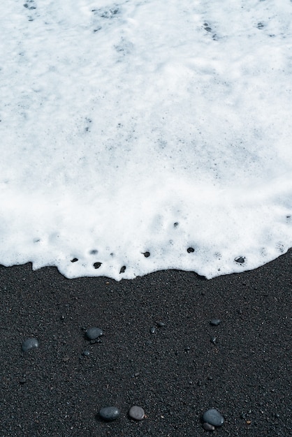 Free photo oceanic wave with white foam rolls over black sand beach with pebble. tenerife volcanic sandy shore.