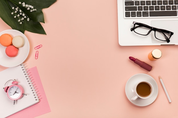 Office desk with macaroons,coffee cup,makeup product,eyeglasses on laptop over the peach backdrop