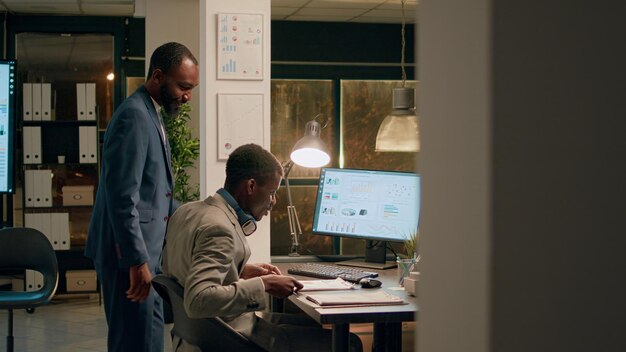 Office manager interrupting unattentive employee listening to music while solving tasks to show him mistake he needs to fix Management executive discussing project results with businessman